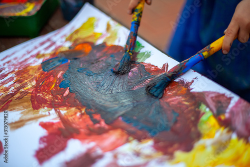 Child at nursery painting with a paint brush in either hand, learning expression and creativity through messy play. Close up of the paint brush strokes being make on the paper.