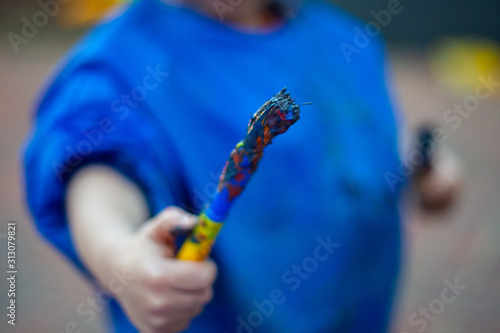 Child at nursery holding paint brushes in either hand, learning colour and creativity through messy play. Close up of one hand holding a paint brush ready to create a painting.