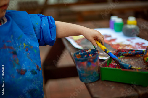 Child at nursery painting with a brush and roller, learning colour and creativity through messy play. Close up of the paints and the child holding a paint brush to create a painting.