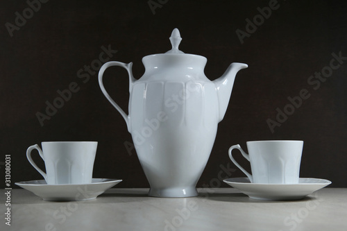 White retro coffee or tea pot with cups on dark background..