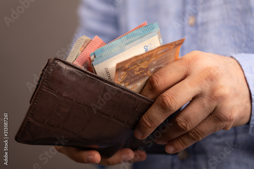 Hands opening a leather wallet with Euro banknotes inside