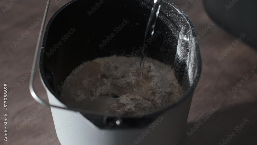 Water Being Poured Into Bread Mixer Container Onto Flour Mix. Close Up, Slow Motion Water Being Poured Into Bread Mixer Container Onto Flour Mix. Close Up, Slow Motion