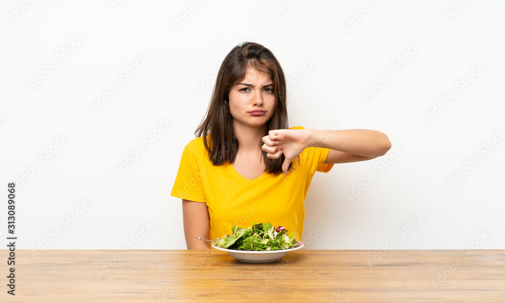 Caucasian girl with salad showing thumb down sign Caucasian girl with salad showing thumb down sign