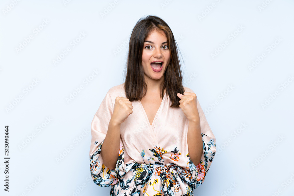 Caucasian girl with kimono over isolated blue background celebrating a victory Caucasian girl with kimono over isolated blue background celebrating a victory