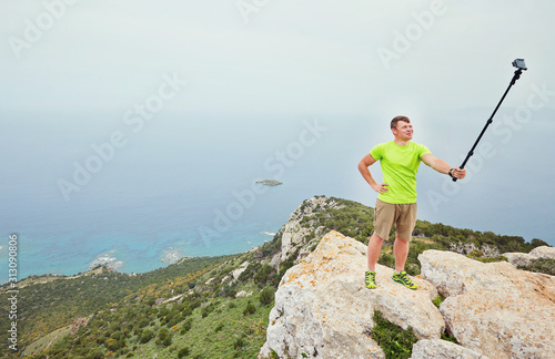 A tourist at the top of a mountain takes a selfie on an action camera.