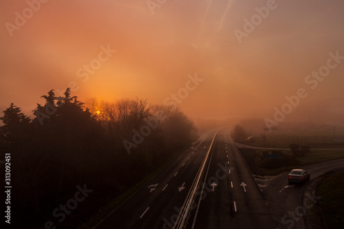 morning fog on the highway and beautiful sky in orange red. setting sun and low fog in winter.