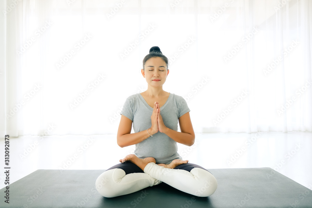 Asian woman sitting on mat and doing yoga and raise hand or pay(namaste) obeisance with legs crossed and eyes closed in room at home,Concept of healing body and spirit. Asian woman sitting on mat and doing yoga and raise hand or pay(namaste) obeisance with legs crossed and eyes closed in room at home,Concept of healing body and spirit.