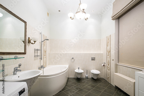 Modern interior of bathroom in light tones with black tile on the floor. Bath  toilet and sink.