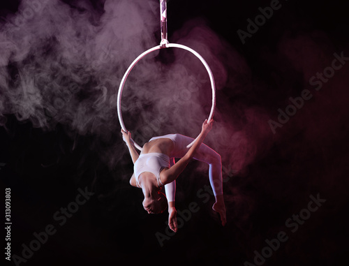 Young woman performing acrobatic element on aerial ring indoors photo