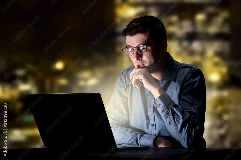 Young handsome businessman working late at night in the office with city lights in the background Young handsome businessman working late at night in the office with city lights in the background