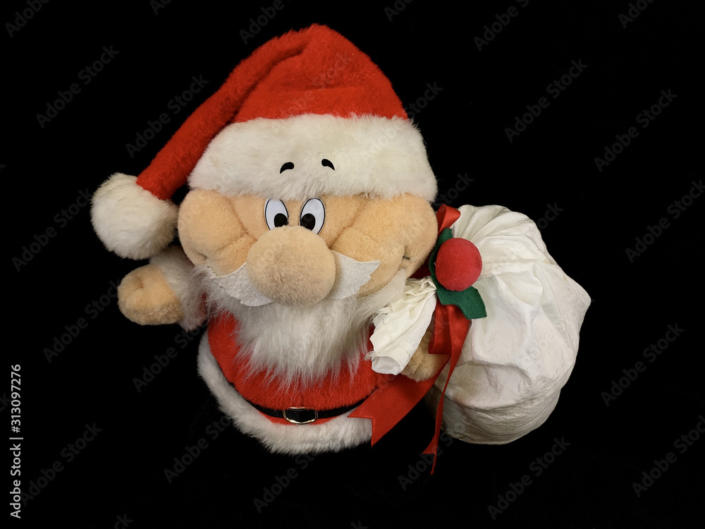 Soft, Christmas toy Santa on a black background. Bright Santa Claus doll with gifts in a bag. Preparation for the holidays, New Year's gifts for children.