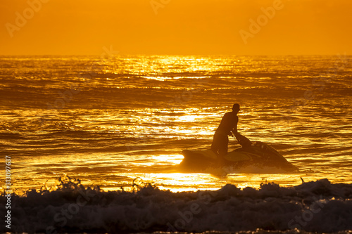 Silhouette of young man riding a water scooter and looking towards the sunrise on the horizon of a beautiful beach