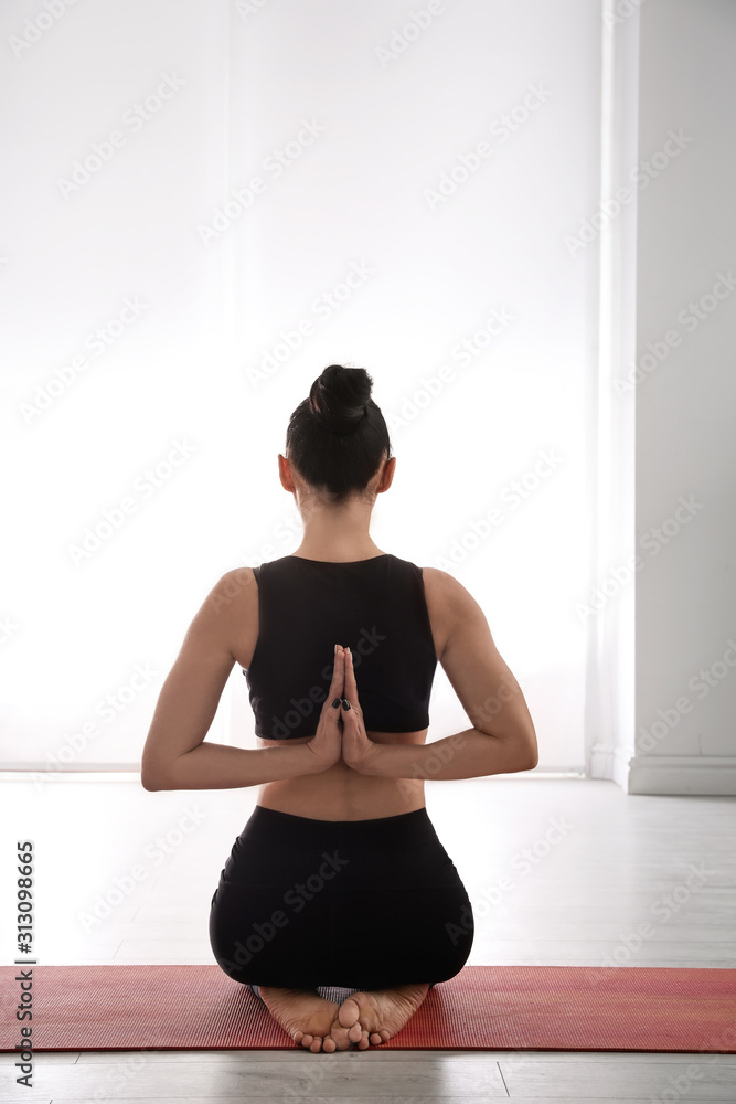 Fototapeta premium Woman practicing vajrasana with namaste behind back in yoga studio