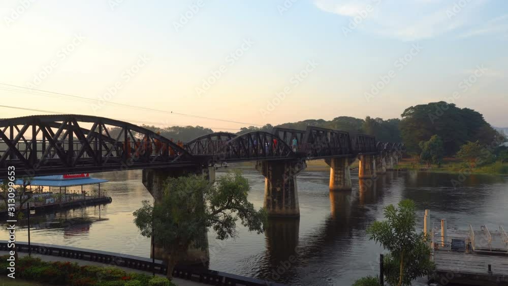 Bridge over the River Kwai in morning time with tourists and monks walking on the bridge. Is an important landmark and a tourist destination Bridge over the River Kwai in morning time with tourists and monks walking on the bridge. Is an important landmark and a tourist destination