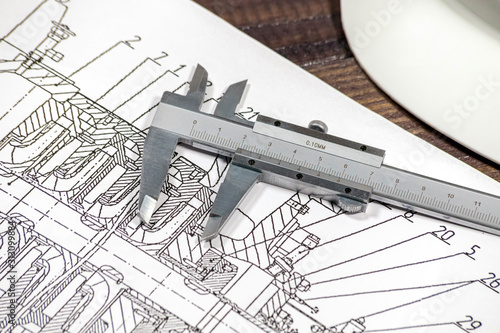 Some pump blueprints on a wooden desk with hardhat and calipers.