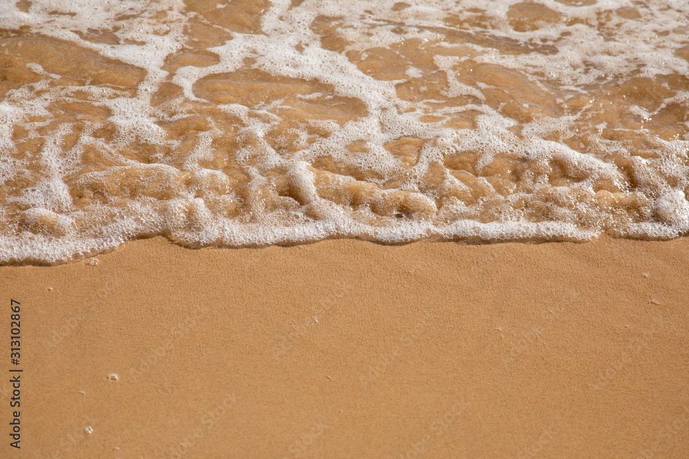 Waves breaking on an empty sand beach and spalsh producing foam - travel holiday vacation summer sun - splashing water - wavy golden yellow sand background - empty space