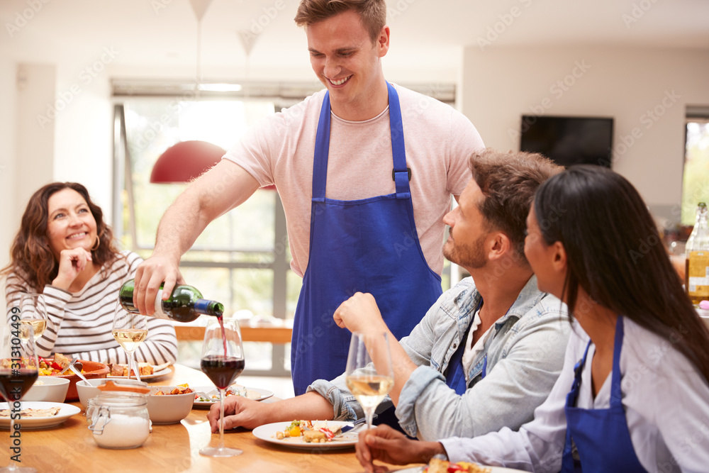 Man Pouring Wine For Group Of Friends Sitting Around Table Eating Meal At Home Together Man Pouring Wine For Group Of Friends Sitting Around Table Eating Meal At Home Together