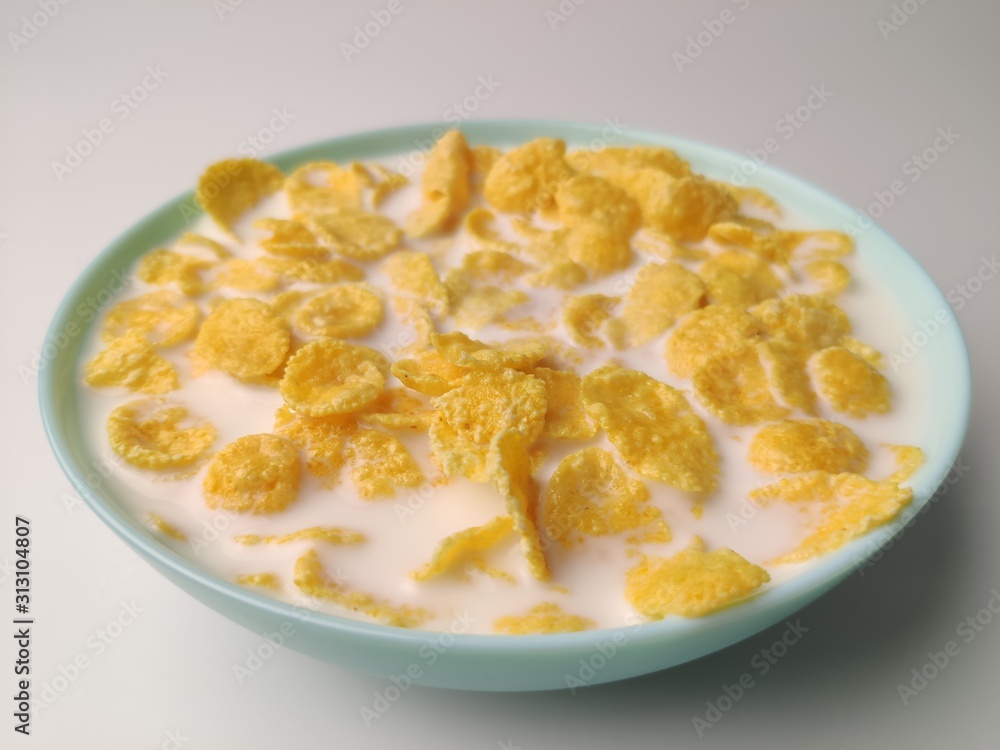 cornflakes with milk in a blue plate on a white background. Delicious healthy Breakfast. cornflakes with milk in a blue plate on a white background. Delicious healthy Breakfast.