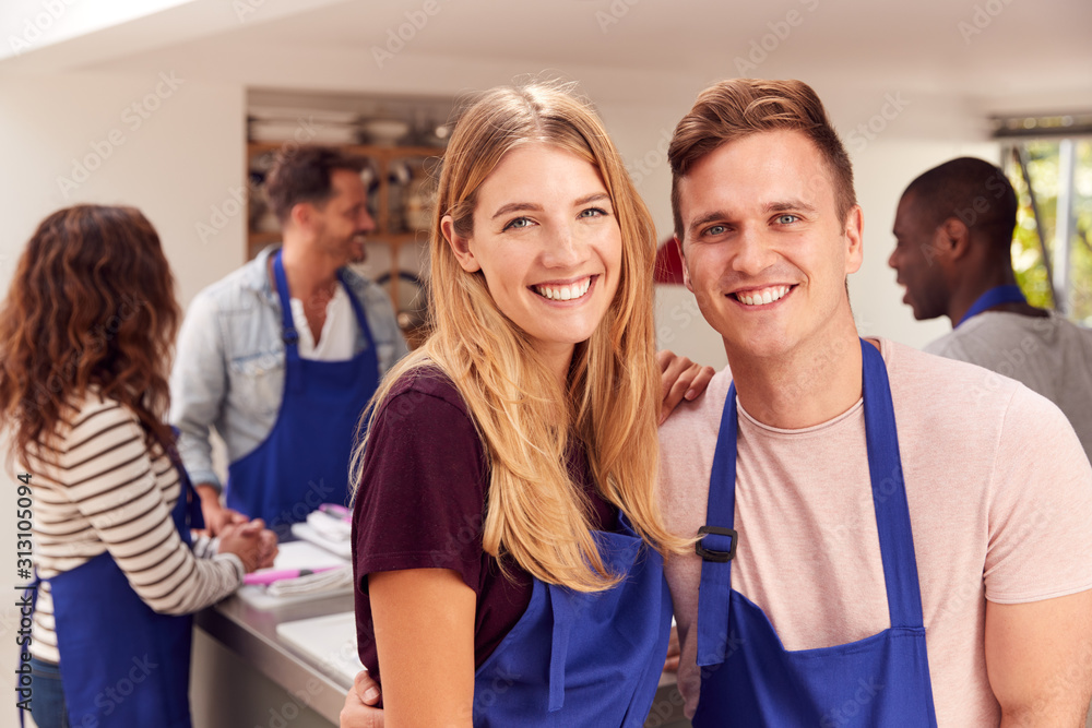 Portrait Of Smiling Couple Wearing Aprons Taking Part In Cookery Class In Kitchen