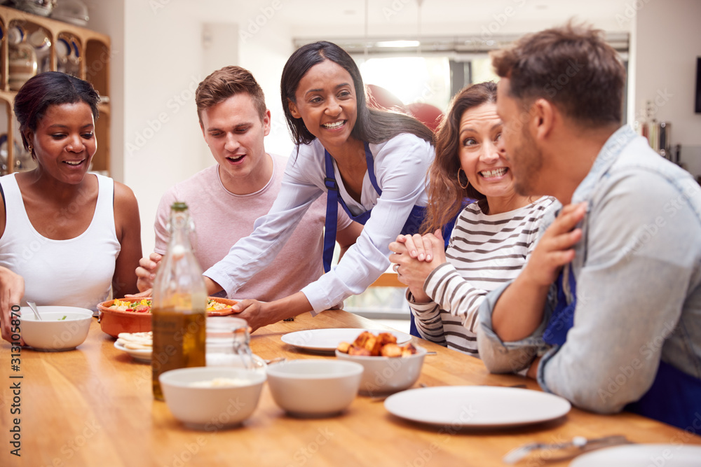 Group Of Friends Sitting Around Table Eating Meal At Home Together
