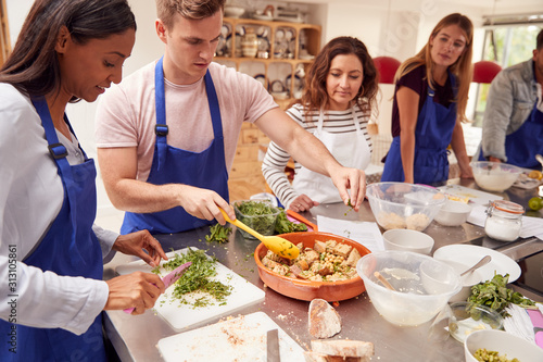 Male And Female Adult Students Preparing Ingredients For Dish In Kitchen Cookery Class