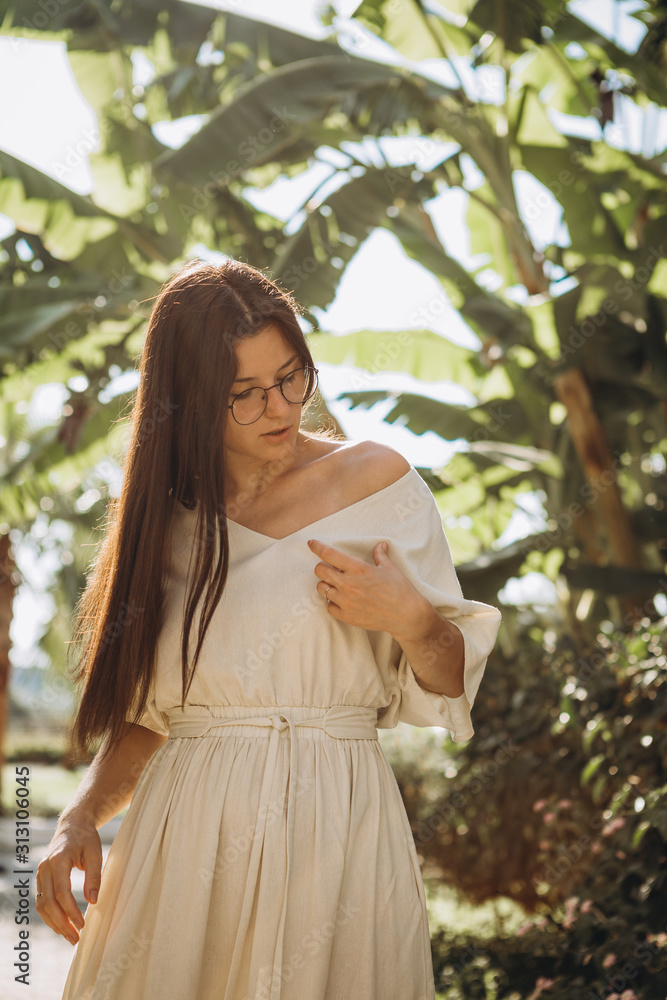 stylish young attractive woman dressed in a long linen dress with a hat photographed in the summer on a background of palm trees and the sea in the bright sun stylish young attractive woman dressed in a long linen dress with a hat photographed in the summer on a background of palm trees and the sea in the bright sun