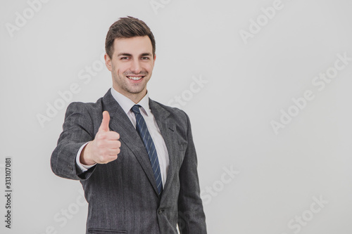 Handsome businessman standing, giving thumb up, smiling, showing his satisfaction.