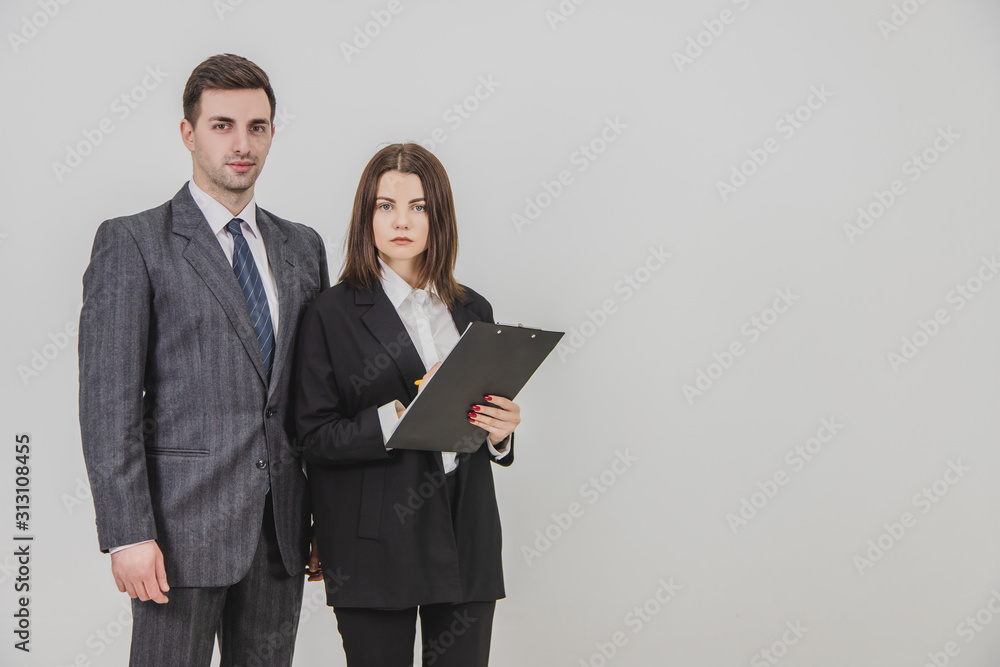 Business partners wearing office suits, standing side by side, looking ar the camera, smiling. Woman holds a clipboard. Business partners wearing office suits, standing side by side, looking ar the camera, smiling. Woman holds a clipboard.