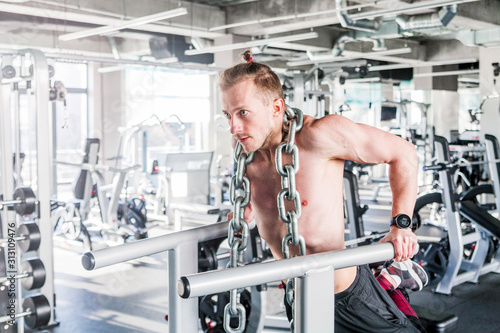 Sportsman with a huge metal chain around his neck. Push-ups on the uneven bars in the gym