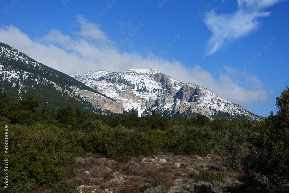 Winter photo of mount Parnitha covered with slight snow and deep blue cloudy sky on a sunny morning