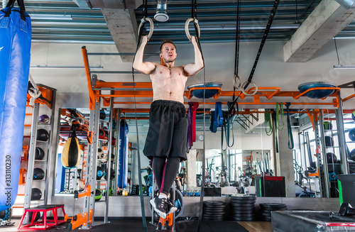 Fitness man is hanging on gymnastics rings in sport hall