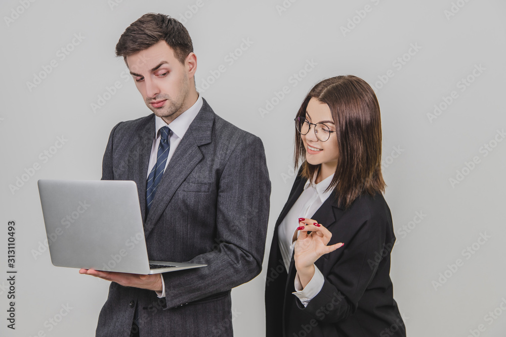 Handsome man standing, working with laptop. Woman is pointing from man's behind at something in the laptop, interfering him. Man is annoyed because of this. Handsome man standing, working with laptop. Woman is pointing from man's behind at something in the laptop, interfering him. Man is annoyed because of this.