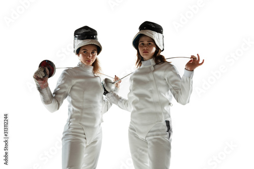 Confidence. Teen girls in fencing costumes with swords in hands on white background. Young female models practicing and training in motion, action. Copyspace. Sport, youth, healthy lifestyle.