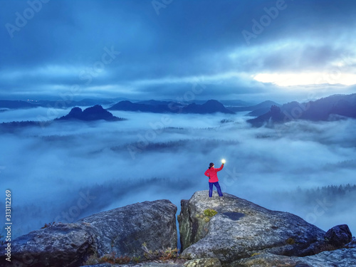 Lost woman hold in hands shining lamp on mountain peak