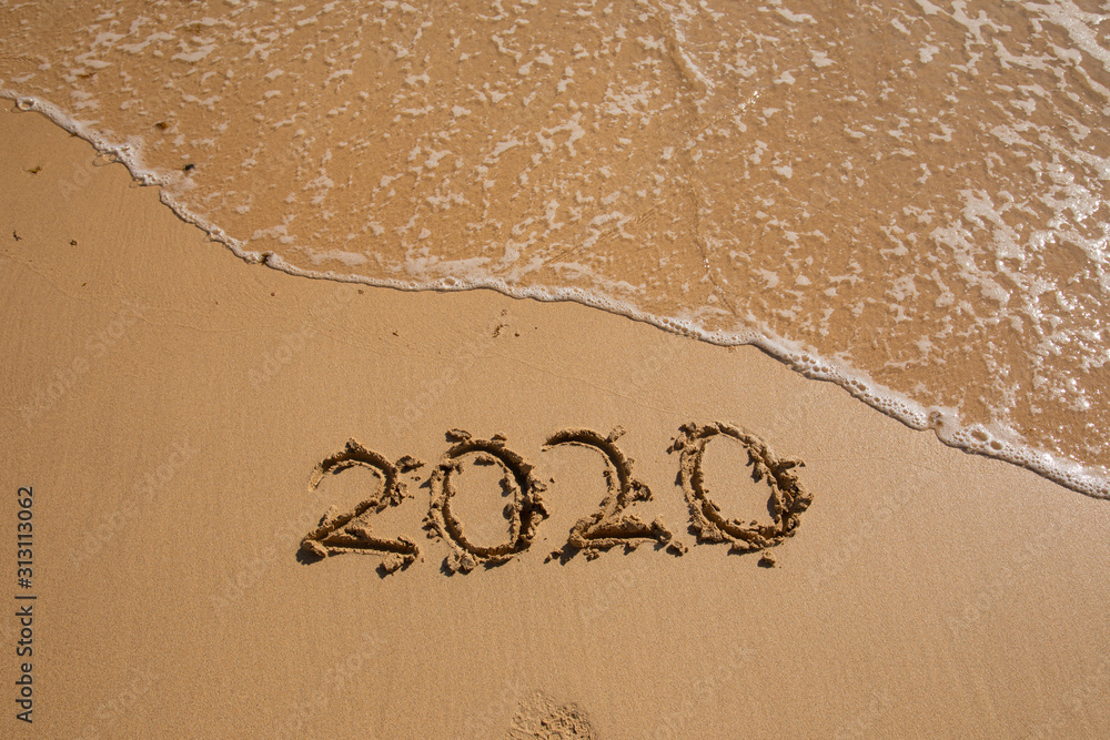 Fototapeta premium Summer beach holiday 2020 season golden sand - year - decade - new season lettering on the beach with wave and clear blue sea. Numbers 2020 year on the sea shore, message handwritten New Years concept