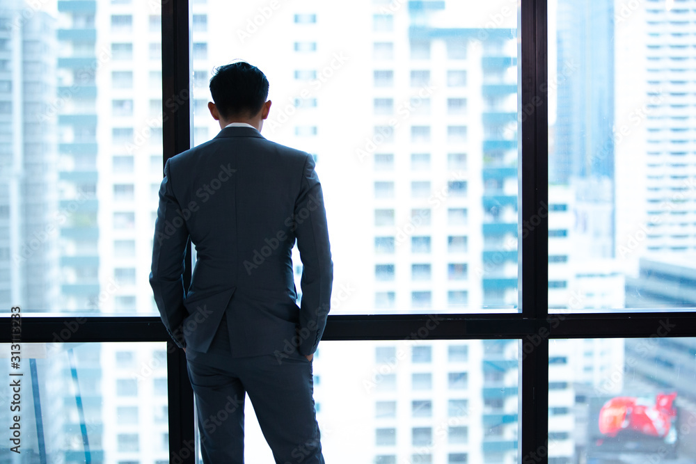 Mature businessman looking out of a window at the city skyline from an office building Mature businessman looking out of a window at the city skyline from an office building