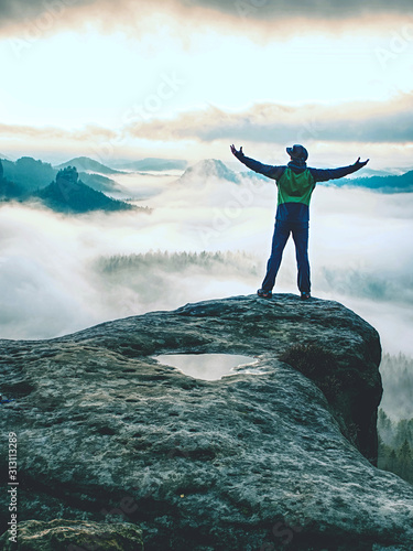 Men on mountain enjoy aerial view, arms raised over clouds