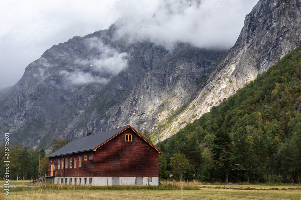 Wooden house in village countryside rocky hills. Mountains near Åndalsnes in Norway, scenic rural nature valley with clouds view. 