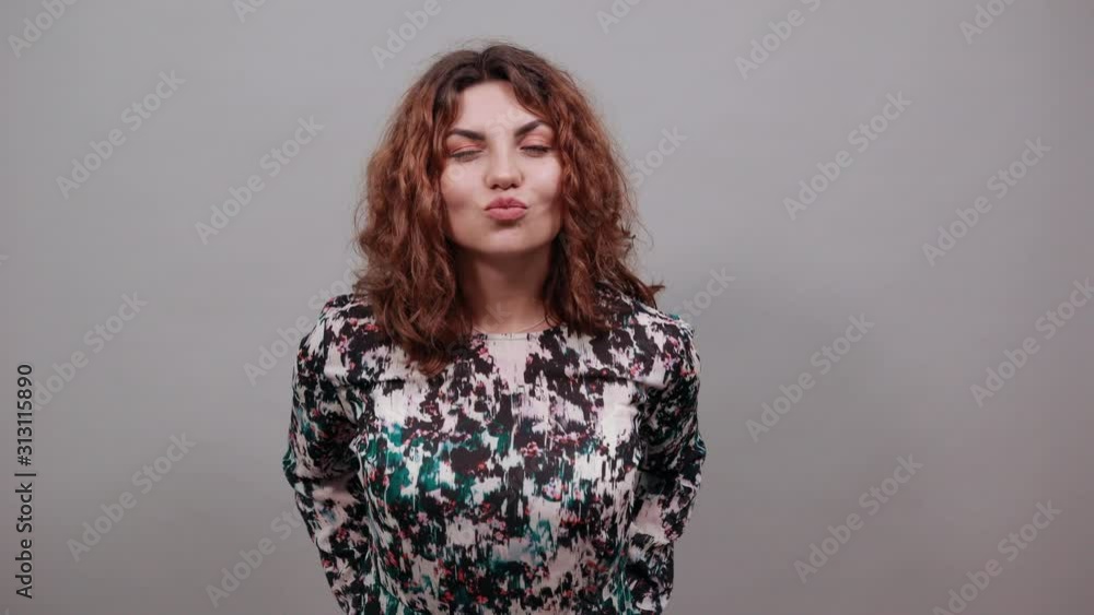 Beautiful brunette woman poved lips, blowing, send air kiss, over isolated gray background in fashion shirt. People emotions. Lifestyle concept Beautiful brunette woman poved lips, blowing, send air kiss, over isolated gray background in fashion shirt. People emotions. Lifestyle concept