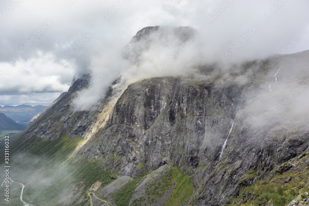 Mountains with waterfall and clouds falling from rocky hills view on Trolls Path Trollstigen road in Norway Europe