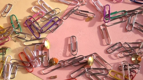 Gold thumbtacks slowly fall onto multicolored paper clips lying on the white table, background, slow motion