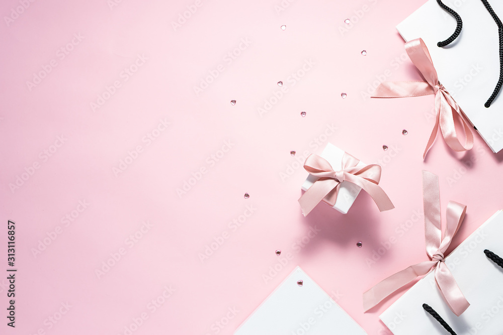 Flat lay overhead composition with gift bags and boxes with pink ribbons and sparkling decorative heart on pink pastel background with copy space for your design. Valentine’s Day concept. 