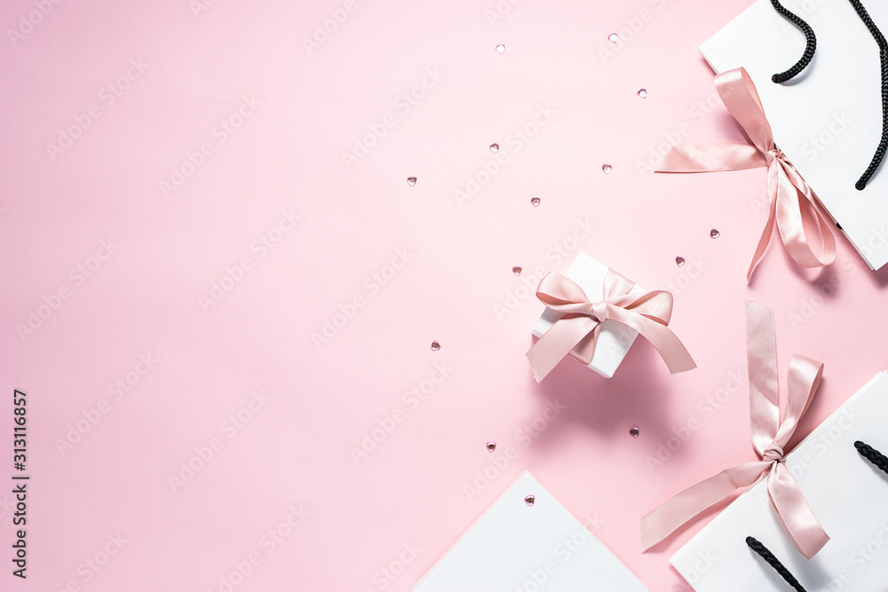 Flat lay overhead composition with gift bags and boxes with pink ribbons and sparkling decorative heart on pink pastel background with copy space for your design. Valentine’s Day concept. Flat lay overhead composition with gift bags and boxes with pink ribbons and sparkling decorative heart on pink pastel background with copy space for your design. Valentine’s Day concept.