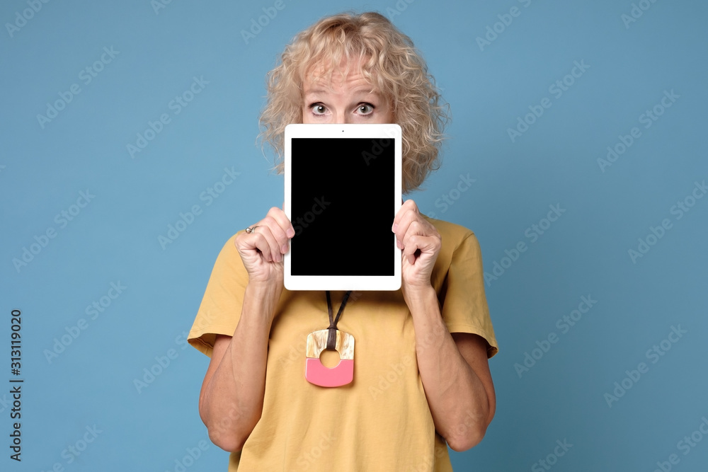 Tablet face. Mature woman hiding his face behind portable computer device on blue background