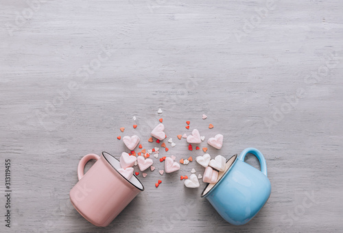 two mugs of blue and pink lie on their side, small candy hearts and marshmallow hearts spilled out