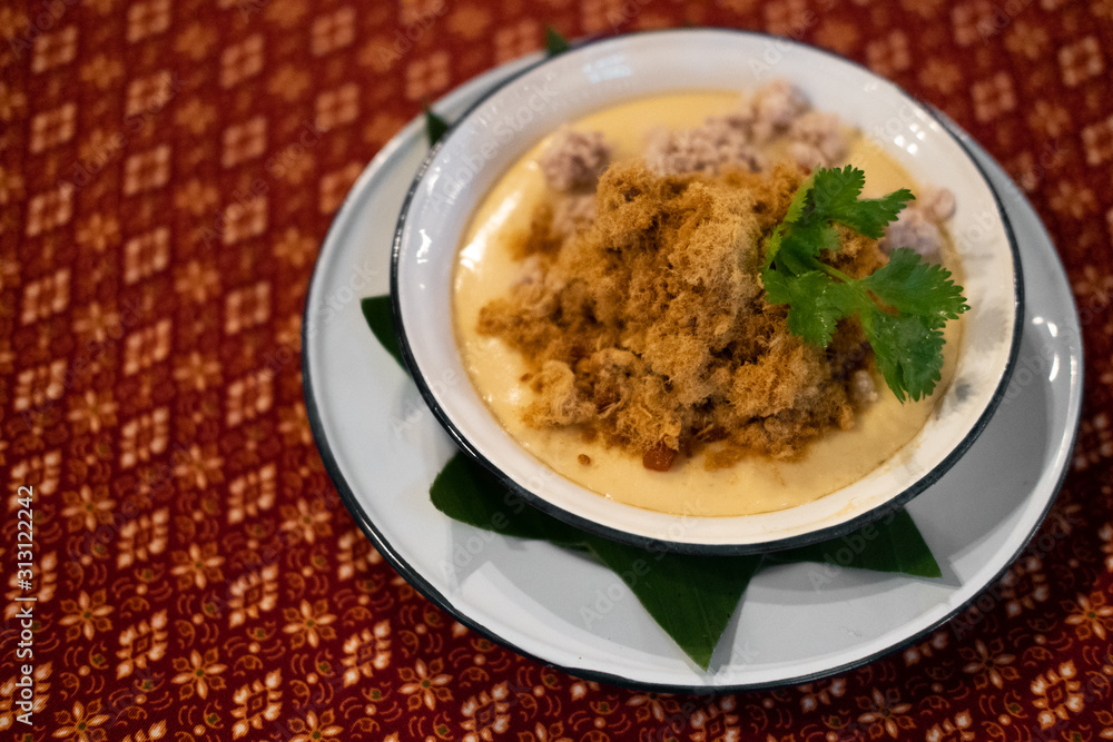 Steamed egg with dried shredded pork in the white bowl on the Thai pattern fabric Steamed egg with dried shredded pork in the white bowl on the Thai pattern fabric