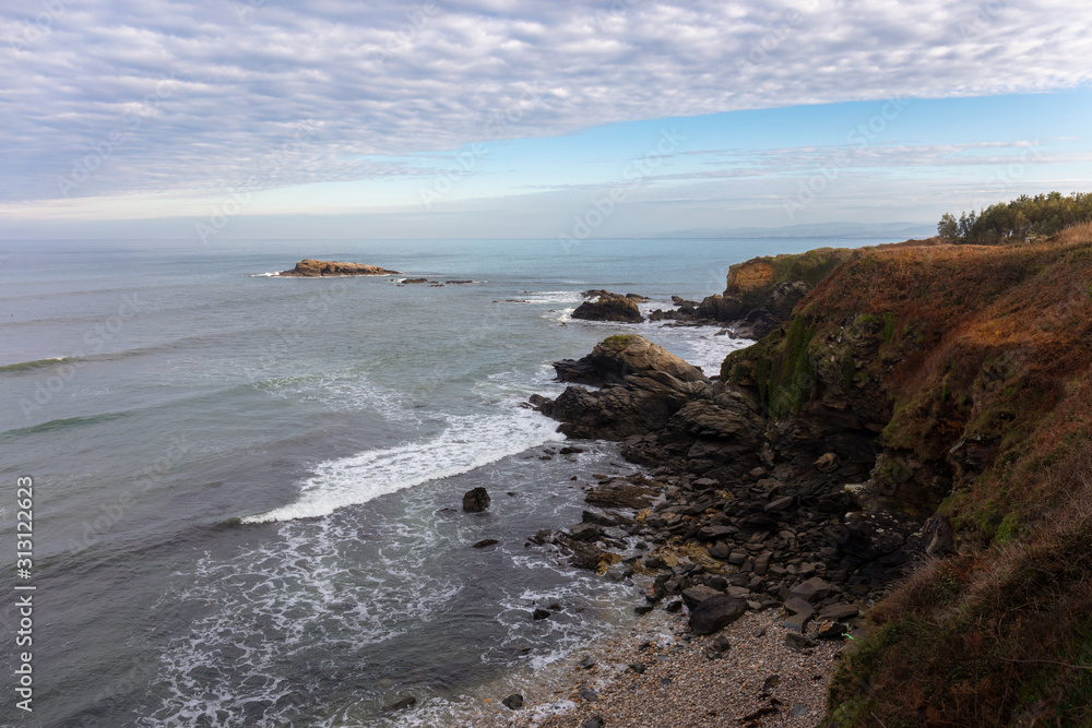 The beautiful rugged Atlantic coast in northern Spain in Galicia near the port city of Foz. Waves roll into the bay. A nice winter day with sunshine and clouds.