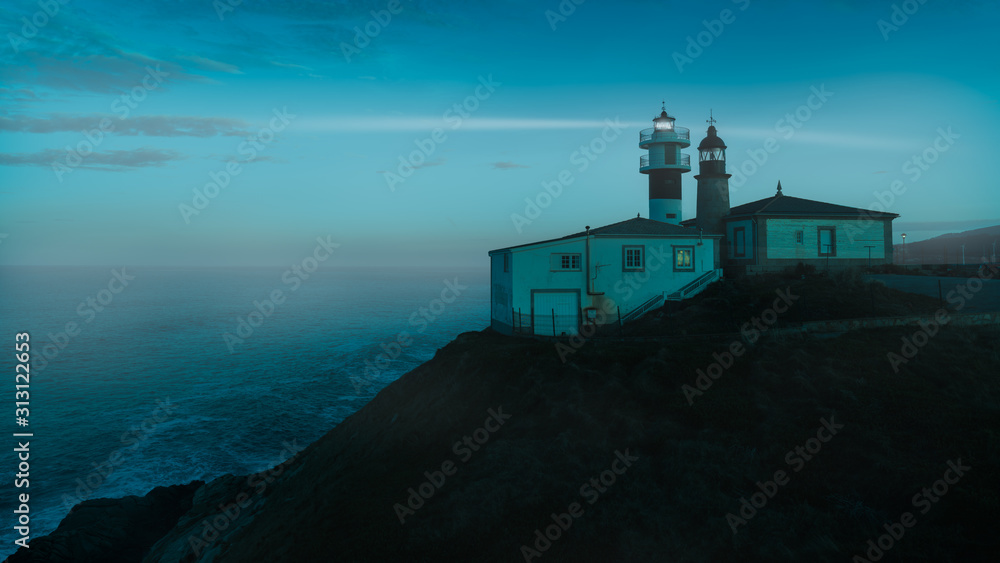 After sunset at the double lighthouse of Punta Atalaia on the north coast of Spain in Galicia on the Atlantic. It is foggy and the coast and the rays of light can be seen in the moonlight.