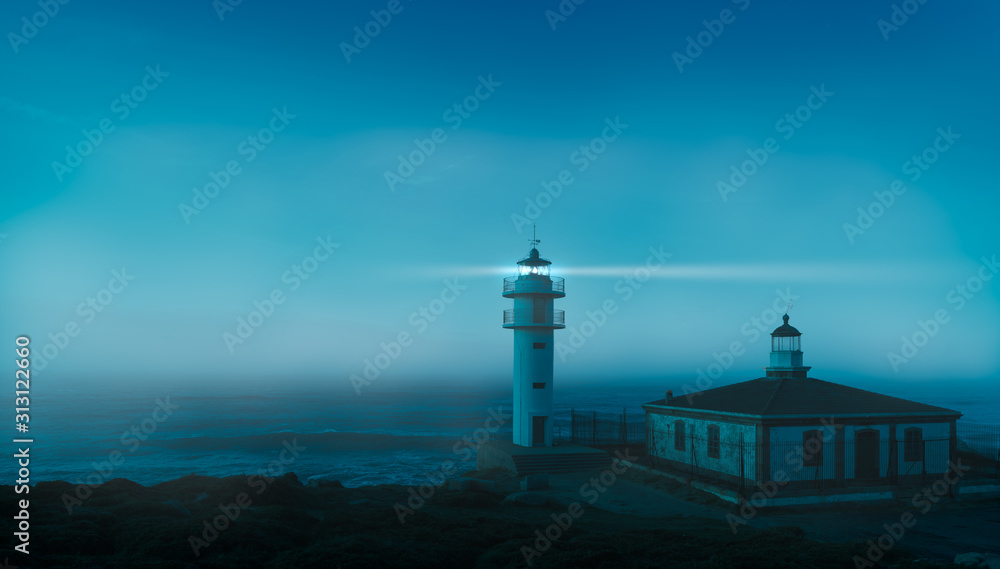 After sunset Tourinan lighthouse on the north coast of Spain in Galicia on the Atlantic. It is foggy and the coast and the rays of light can be seen in the moonlight.