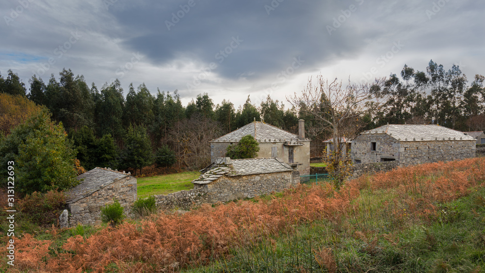 An old uninhabited farm in Galicia in northern Spain. The stone houses have a Celtic style and are very old. It is a cold winter day with dark clouds in the sky. An old uninhabited farm in Galicia in northern Spain. The stone houses have a Celtic style and are very old. It is a cold winter day with dark clouds in the sky.